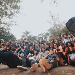 Grupo diverso de pessoas reunido ao ar livre, próximo a plantas, olhando para a câmera
