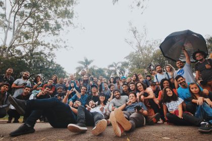 Grupo diverso de pessoas reunido ao ar livre, próximo a plantas, olhando para a câmera