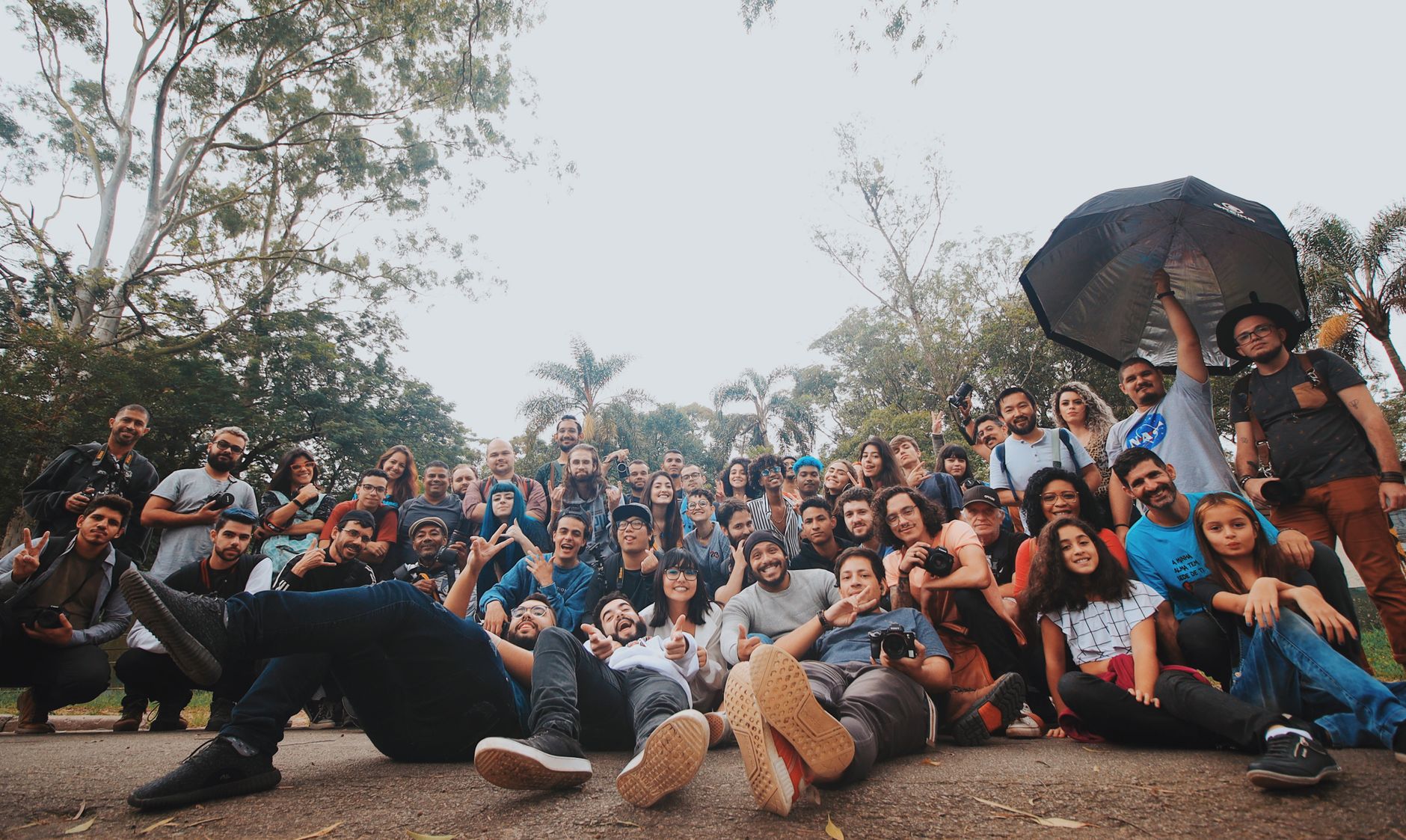 Grupo diverso de pessoas reunido ao ar livre, próximo a plantas, olhando para a câmera