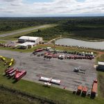 Vista aérea de uma base de combate a incêndios com caminhões, helicópteros e aviões preparados para a ação.