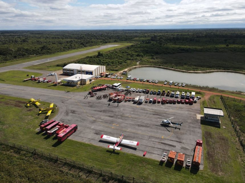 Vista aérea de uma base de combate a incêndios com caminhões, helicópteros e aviões preparados para a ação.
