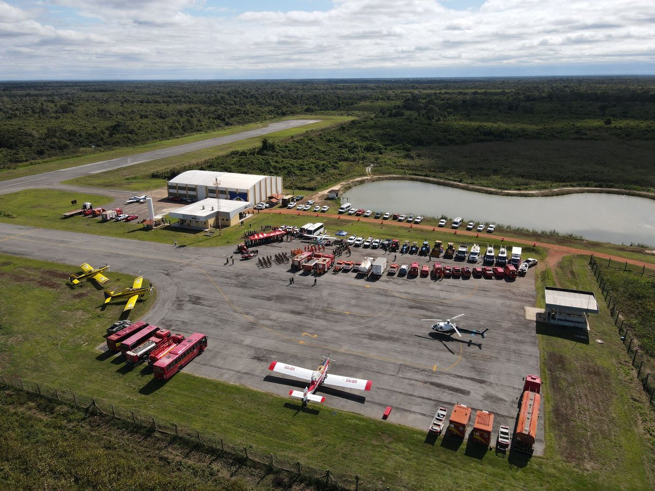Vista aérea de uma base de combate a incêndios com caminhões, helicópteros e aviões preparados para a ação.