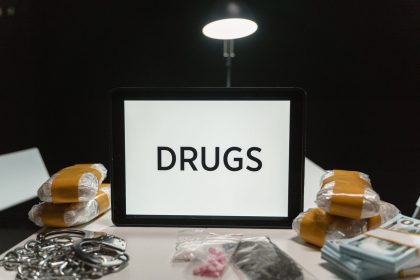 Algemas ao lado de drogas embaladas e dinheiro sobre uma mesa, sob iluminação forte.