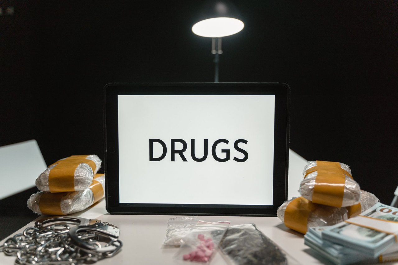 Algemas ao lado de drogas embaladas e dinheiro sobre uma mesa, sob iluminação forte.