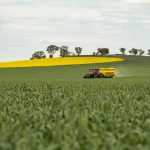 Trator vermelho distribui fertilizante em uma plantação verde sob céu nublado.