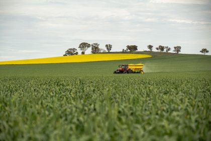 Trator vermelho distribui fertilizante em uma plantação verde sob céu nublado.